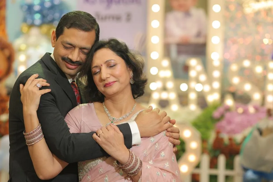 A couple shares an intimate hug at a festive celebration decorated with elegant lights.