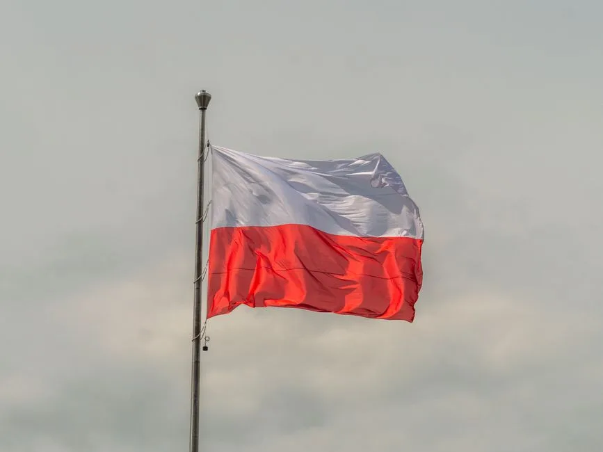 The Polish national flag waving prominently against a cloudy sky, showcasing patriotic pride.