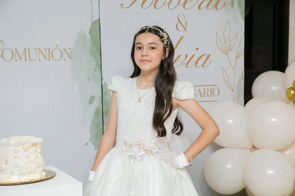 Young girl in elegant First Communion dress with decorations and cake.