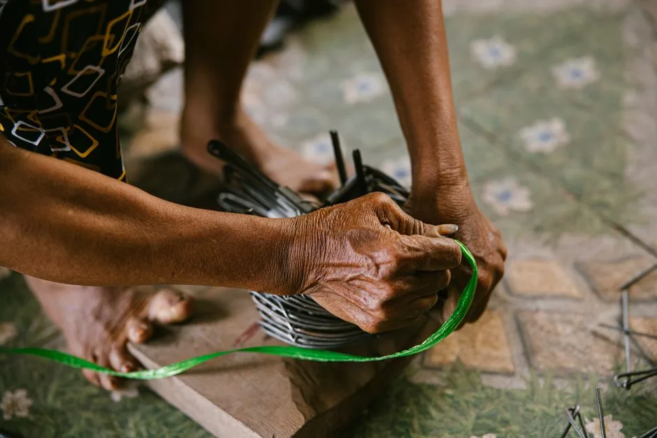 Close-up of hands skillfully crafting with wire on a floral patterned floor, highlighting traditional craftsmanship.