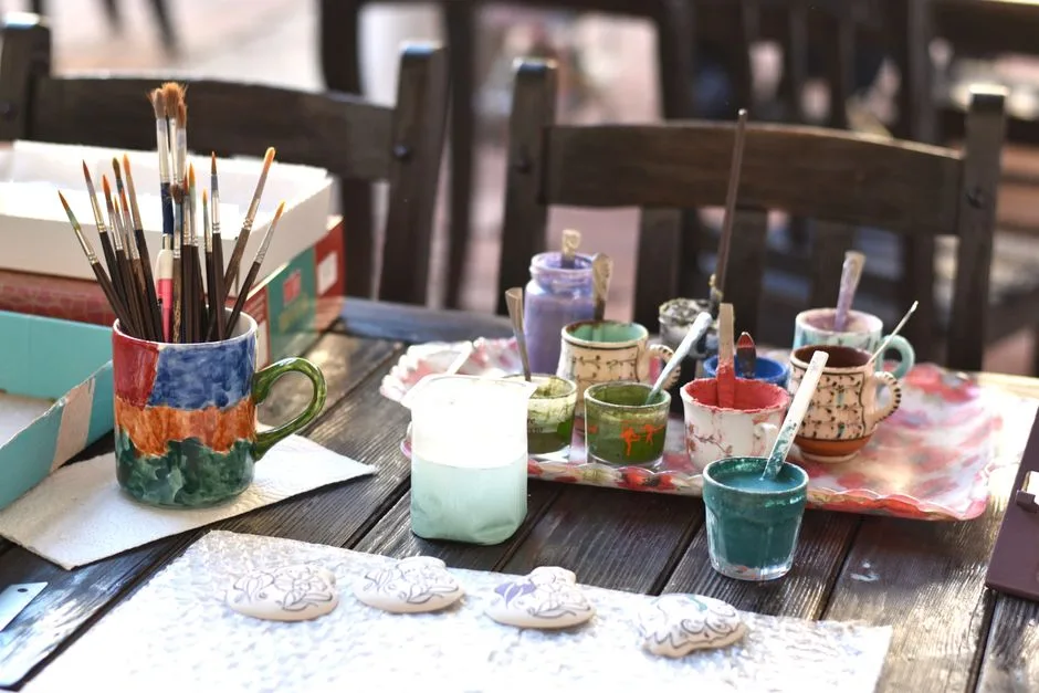 Creative ceramic art setup with paintbrushes and paints on a wooden table.