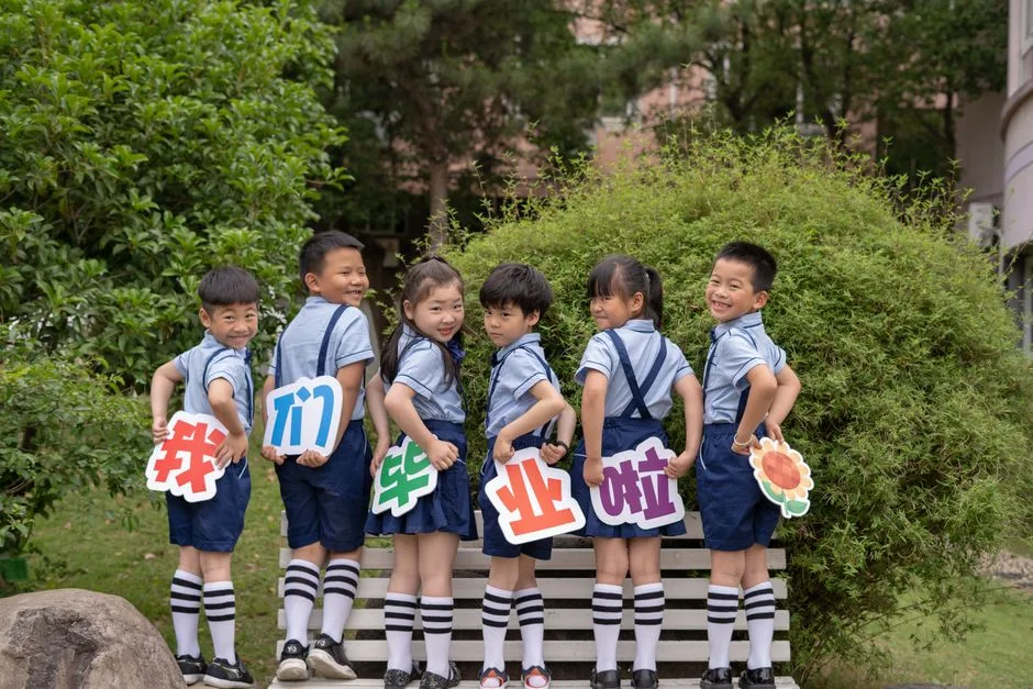 Group of children in uniform holding colorful signs, celebrating graduation outdoors.