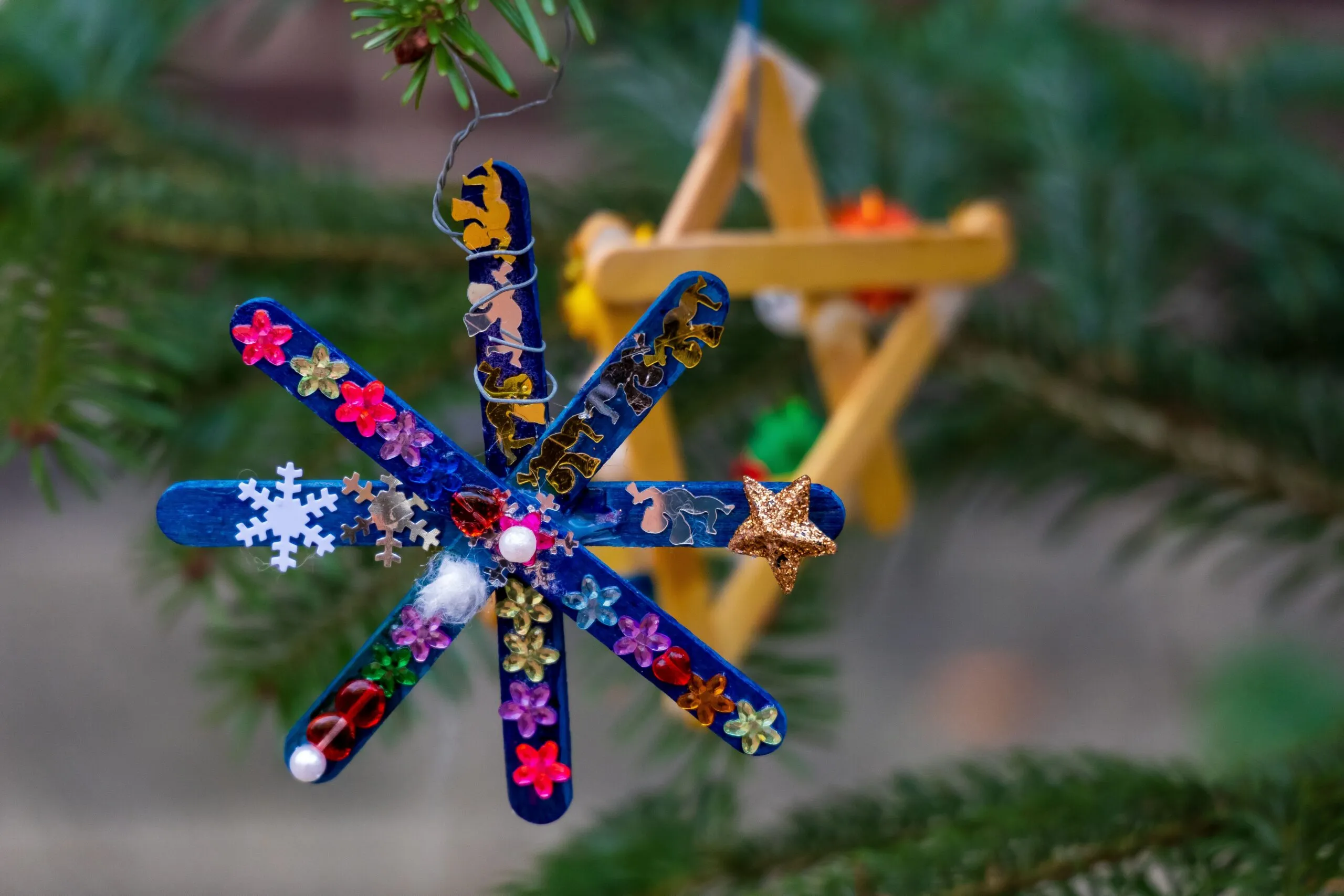 Vibrant handmade popsicle stick ornaments decorate a pine tree, celebrating the holiday season.