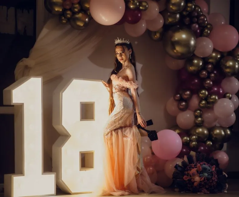 A young woman poses elegantly at her 18th birthday party with glamorous decor.