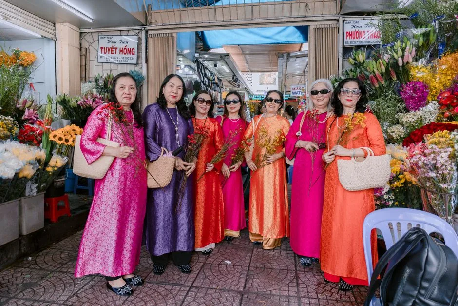 Group of women in ao dai posing in a colorful market with flowers.