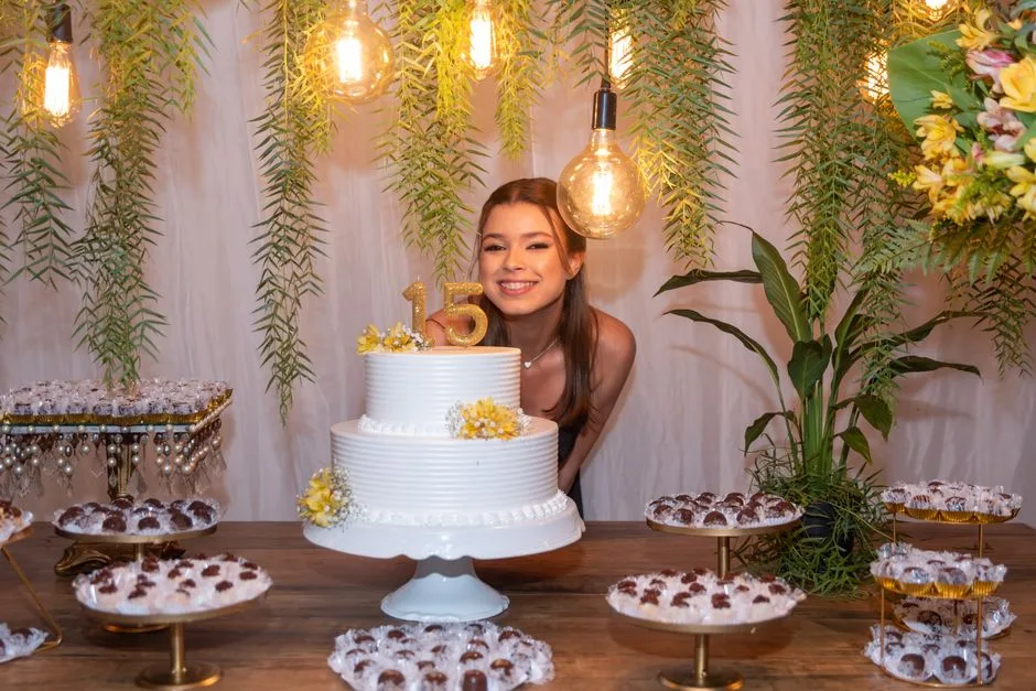 A beautiful indoor quinceañera celebration with cake, floral decor, and a smiling teenage girl.
