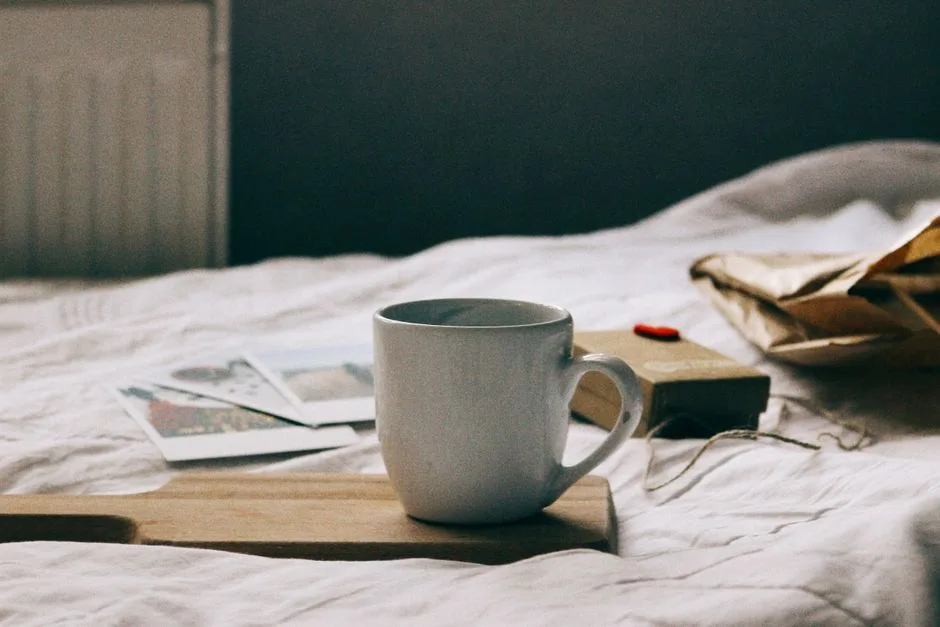 White coffee mug on a wooden tray on bed with soft light and cozy atmosphere.