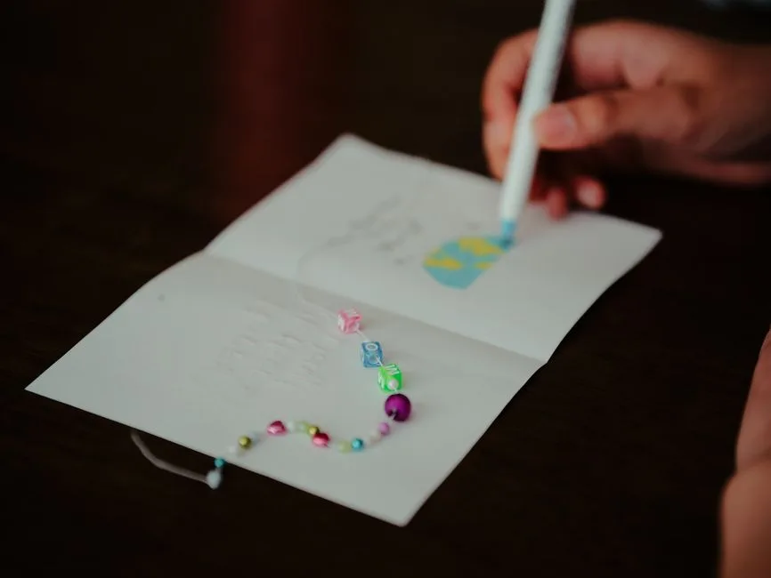 Close-up of a hand decorating a greeting card with colorful beads and a pen, creating a personalized design.