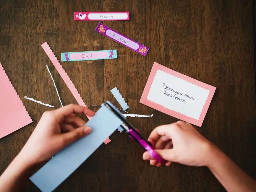 A child creating a personalized Mother's Day card with colorful paper and scissors.