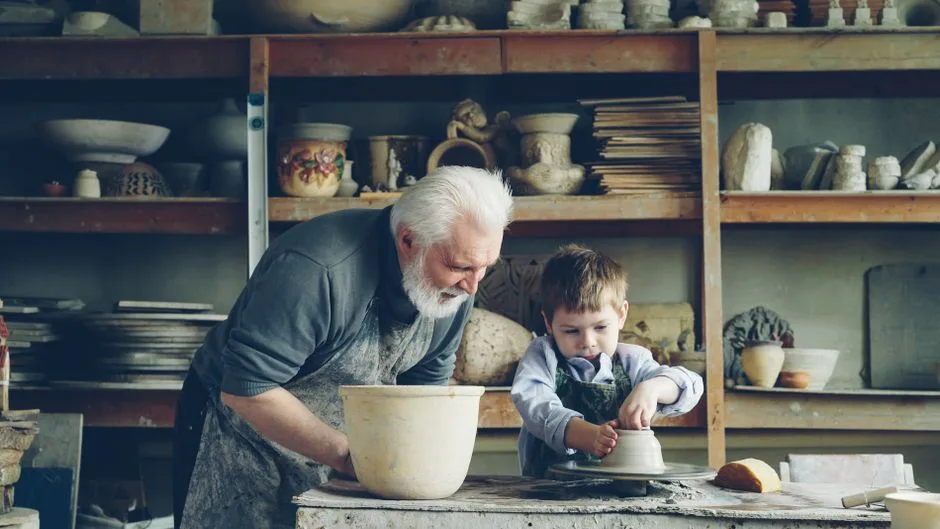 Elderly man and young boy making pottery, highlighting intergenerational learning.