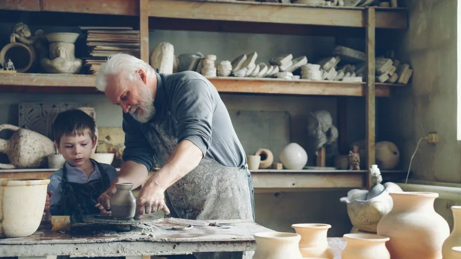 A grandfather and young boy making pottery together in a cozy studio setting.