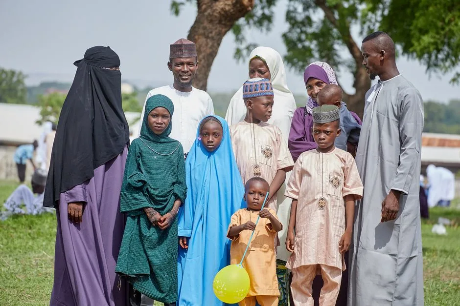 A large family poses together outdoors, enjoying a sunny day with children holding balloons.