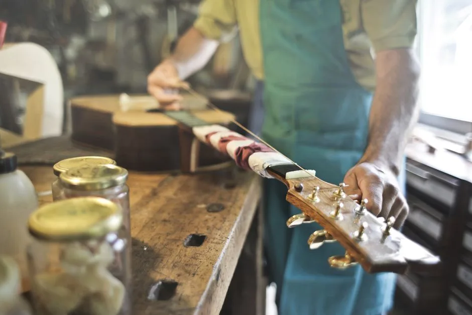 A skilled craftsman works on a guitar in a traditional workshop setting, focusing on details.