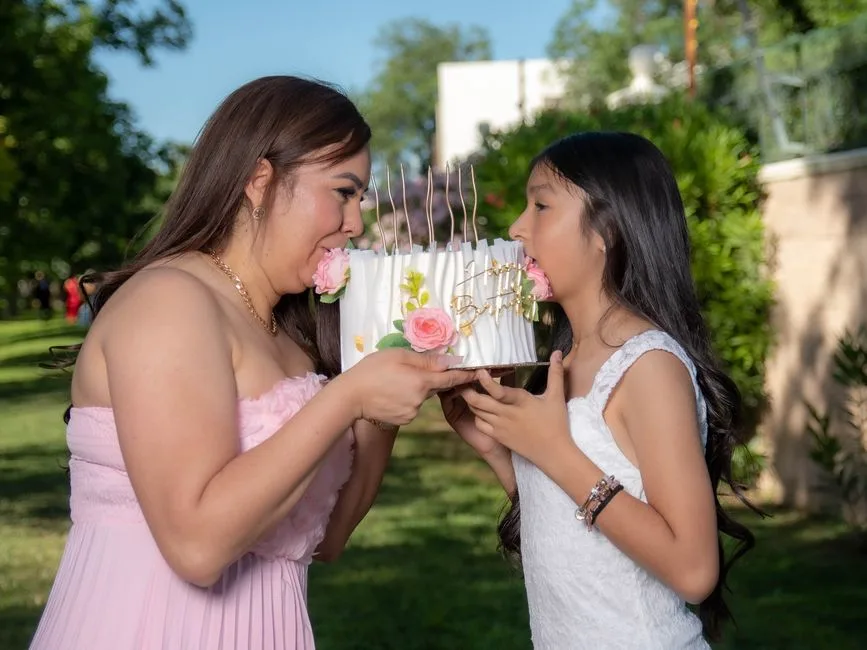 A joyful mother and daughter enjoying a birthday cake together in a sunny outdoor setting.