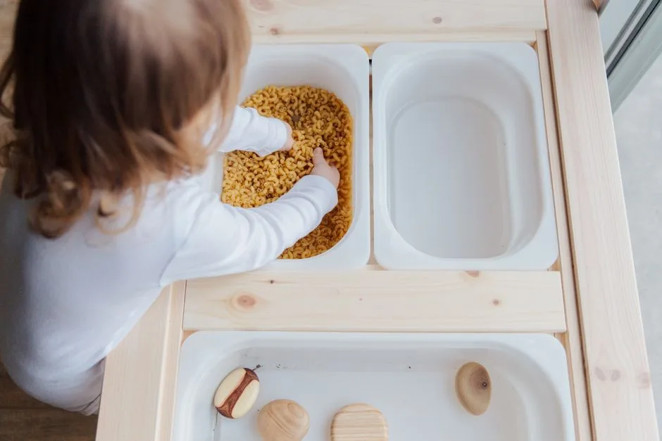 Curious child engaging in sensory play with pasta, exploring textures indoors.