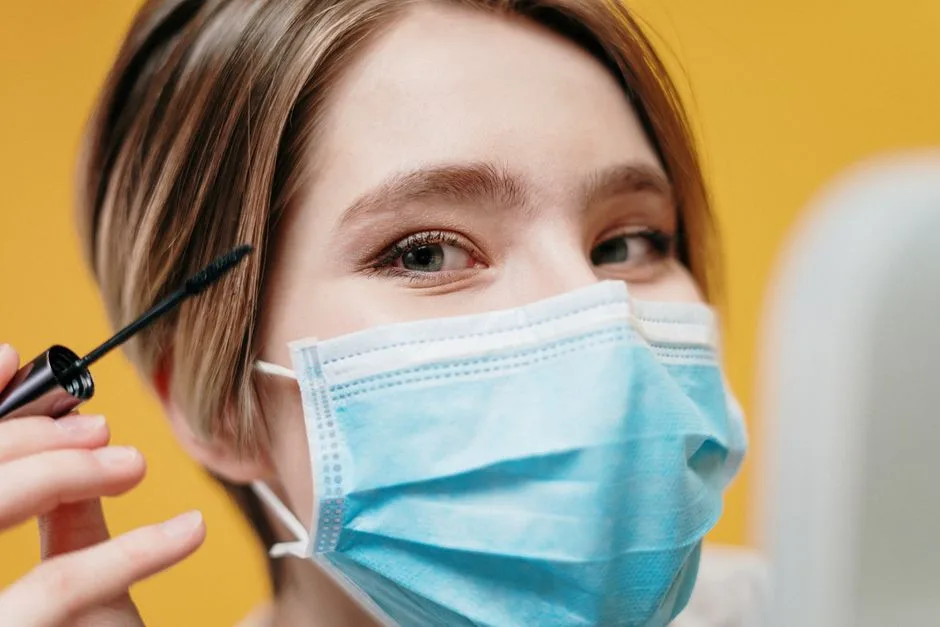 A woman applying mascara while wearing a protective face mask, highlighting beauty and safety.