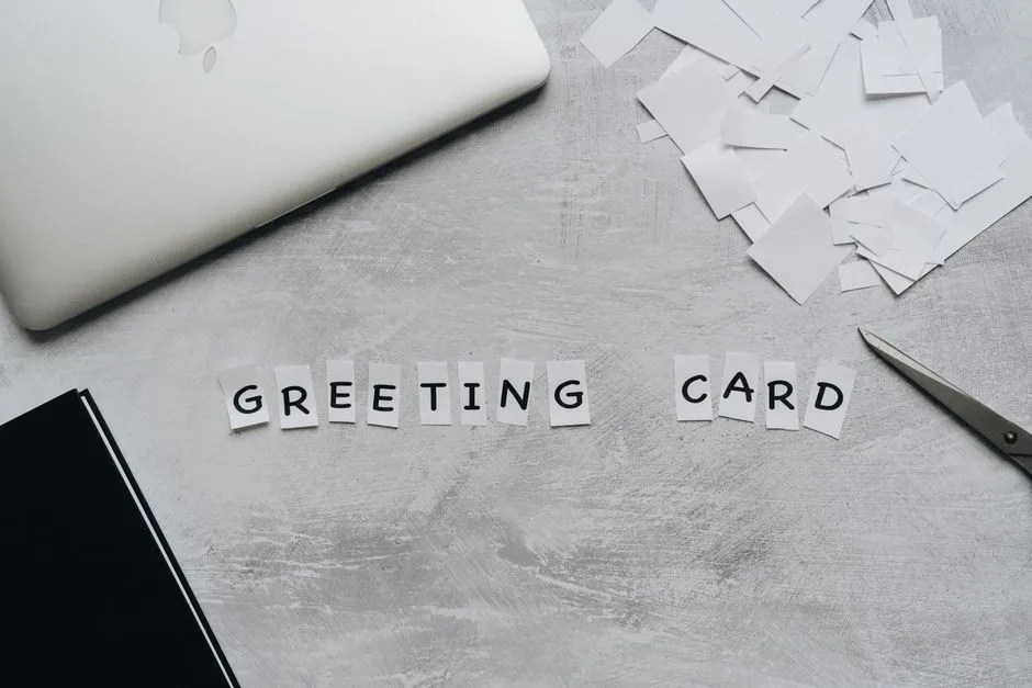 Top view of greeting card arrangement with paper, scissors, and laptop on a gray surface.