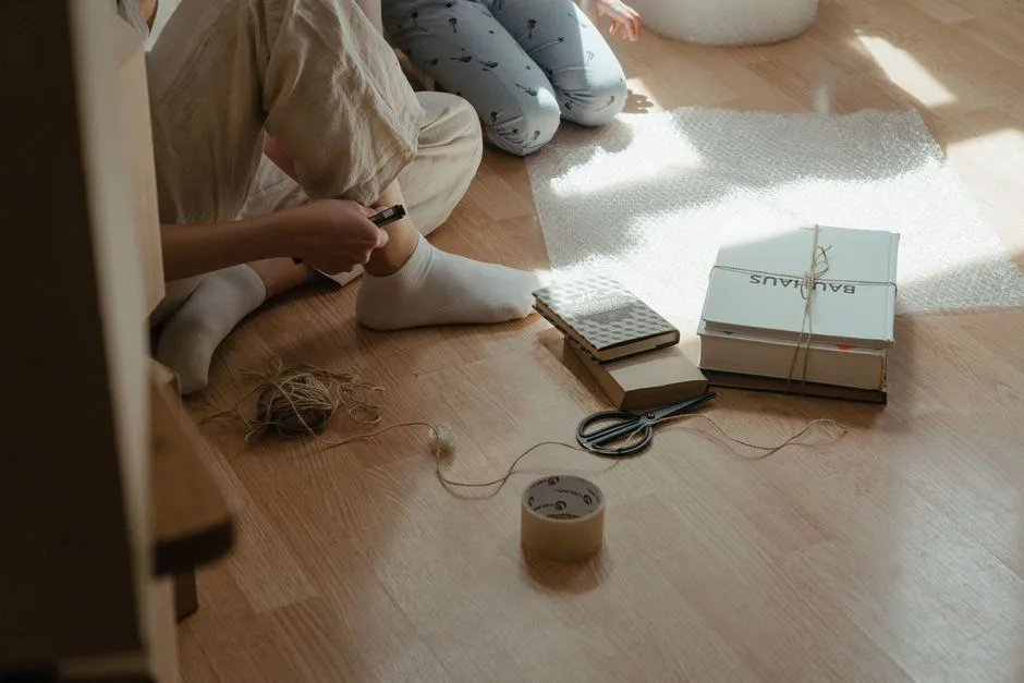 A cozy scene of wrapping books in bubble wrap on a sunlit wooden floor, with tools and materials around.