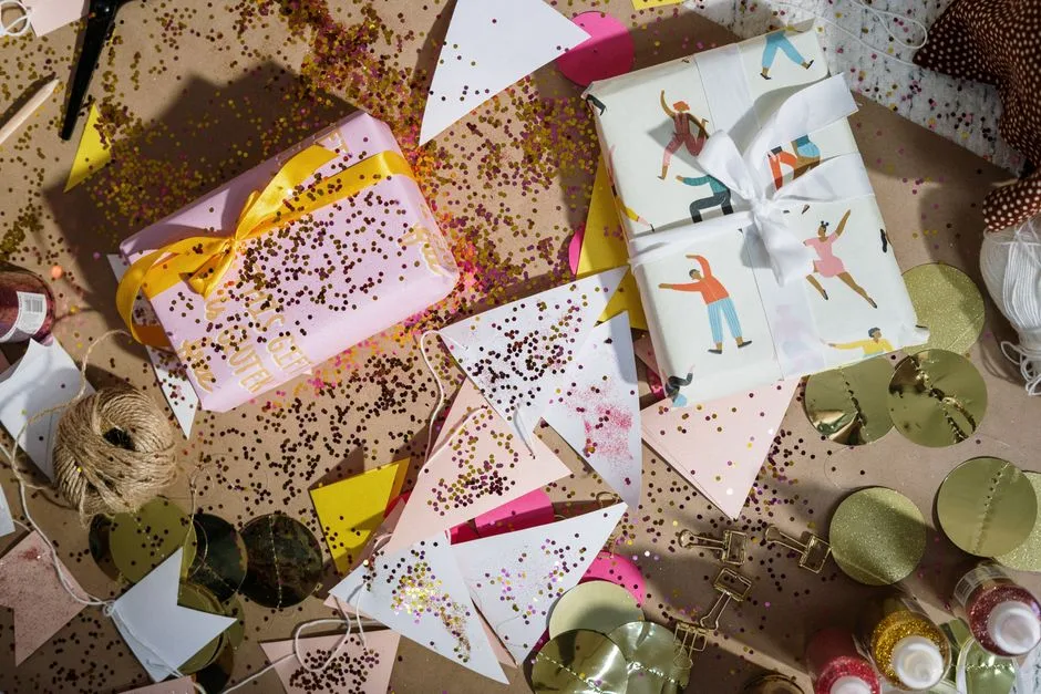 An overhead view of a festive flatlay with wrapped gifts, colorful glitter, and decorations creating a celebration vibe.