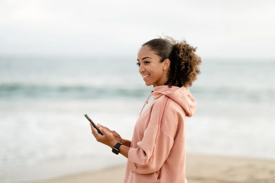 A cheerful woman using a smartphone by the beach, embracing modern technology.