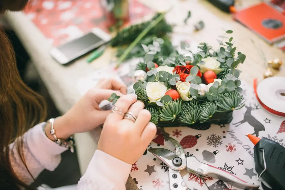 Hands crafting a Christmas floral arrangement with festive decorations.