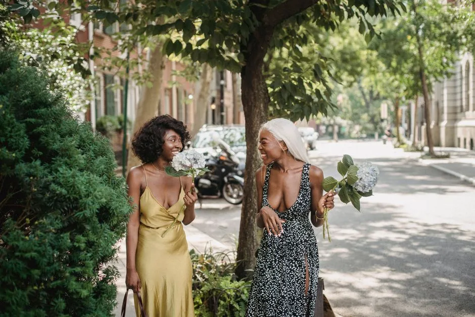 Two women smiling and enjoying a sunny day outdoors, holding bouquets.