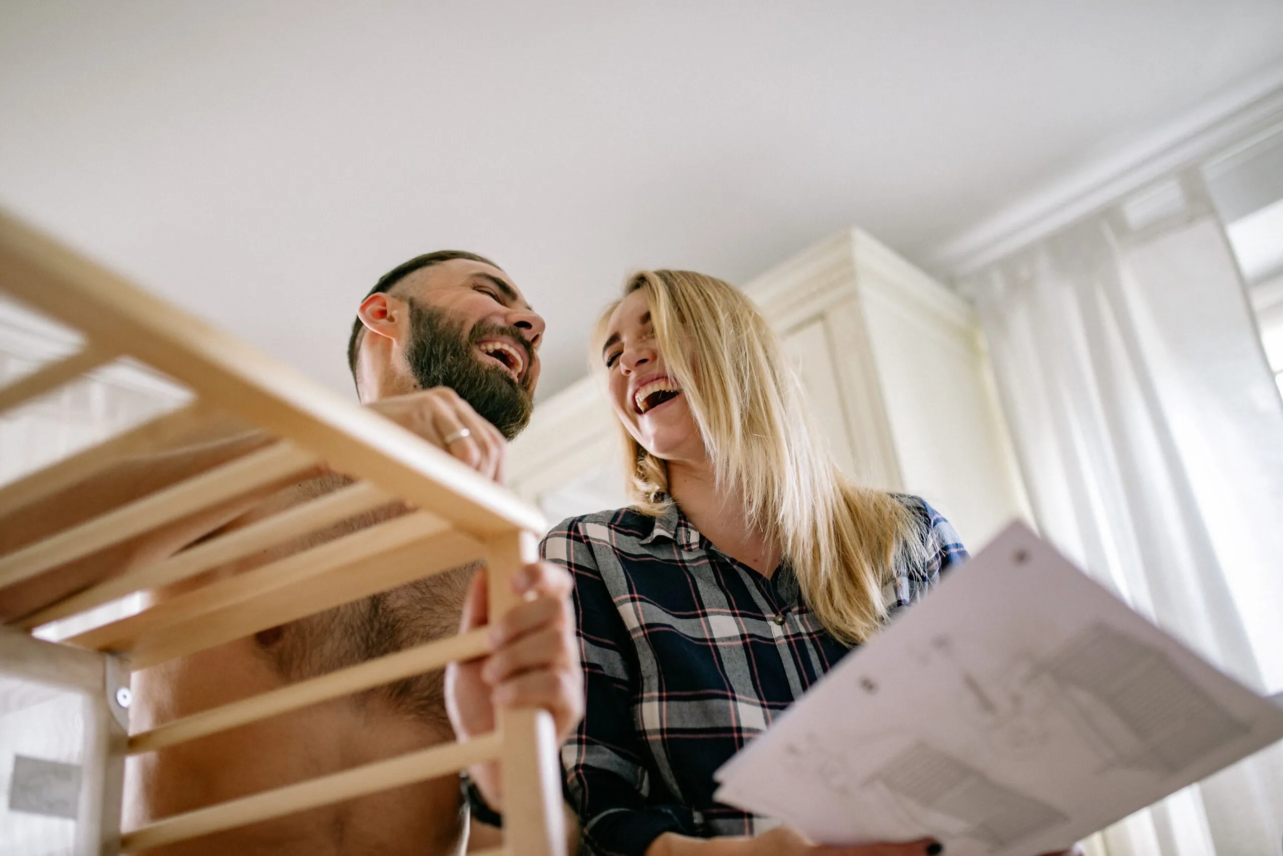 Joyful couple assembling a wooden baby crib at home, preparing for parenthood.