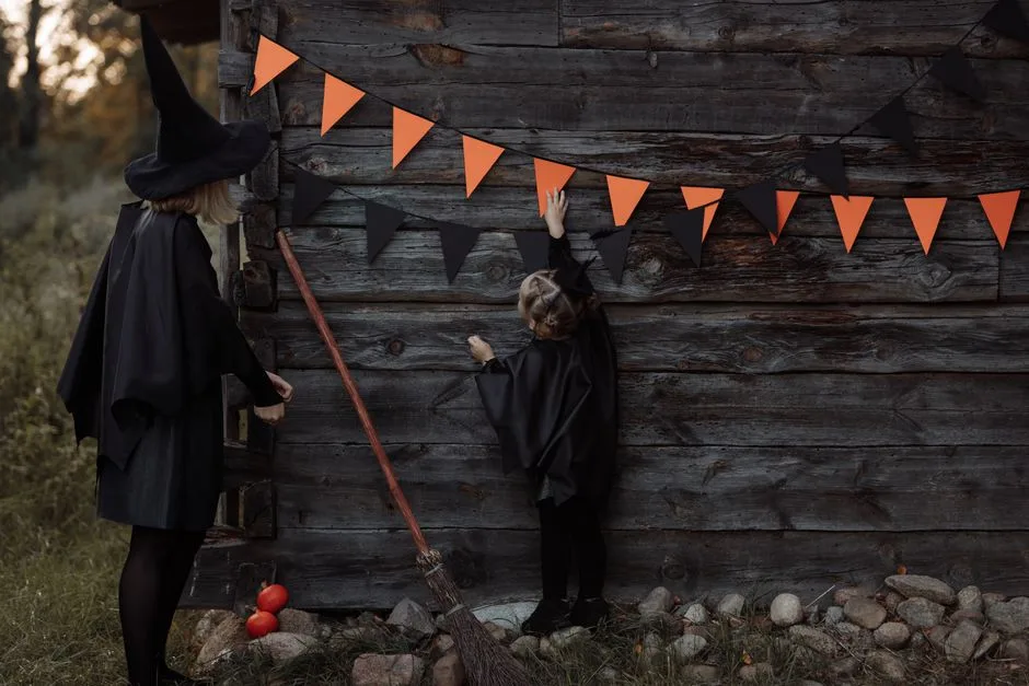 A mother and daughter in witch costumes hang pennant banners on a wooden wall for Halloween.