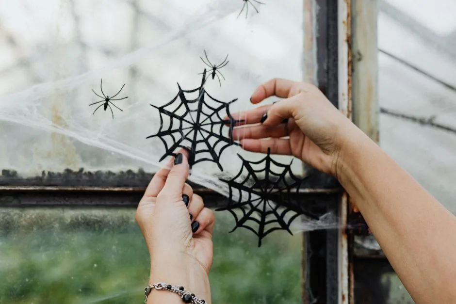 Hands decorating a window with spider web crafts for Halloween, capturing a spooky seasonal vibe.
