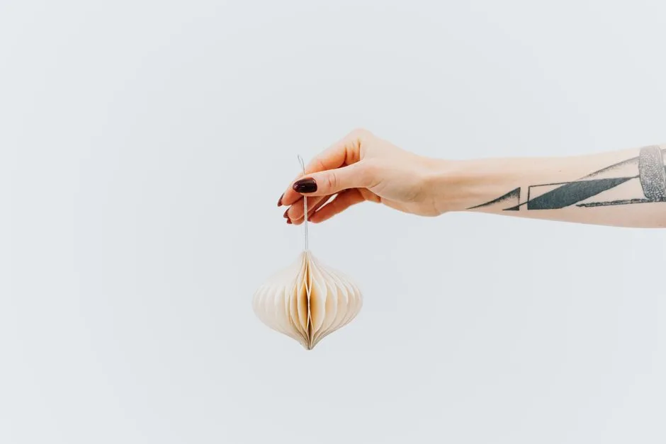 Minimalist image of a hand holding a delicate origami-like Christmas ornament against a white background.