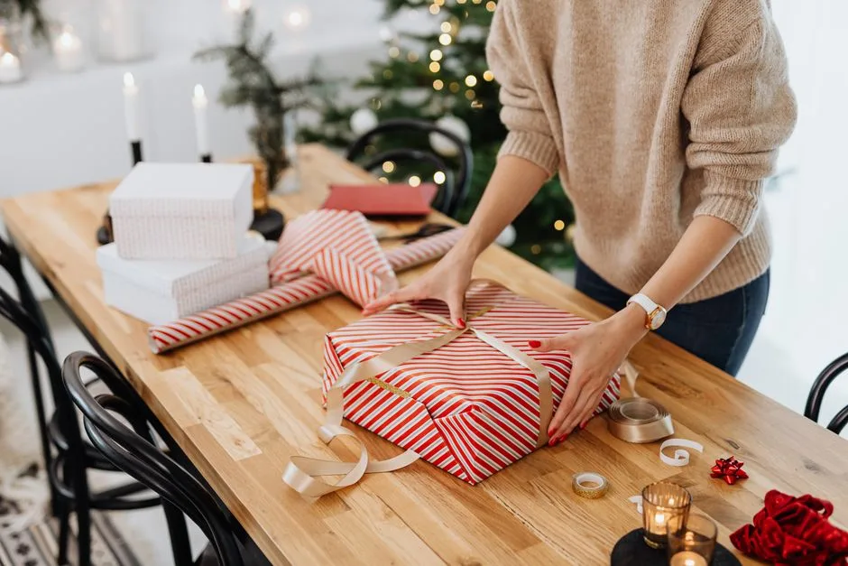Festive holiday scene of a woman wrapping Christmas presents on a wooden table indoors.