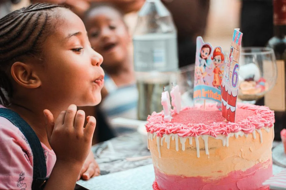 Side view of crop adorable little black girl with Afro braids blowing out candles on birthday cake during party