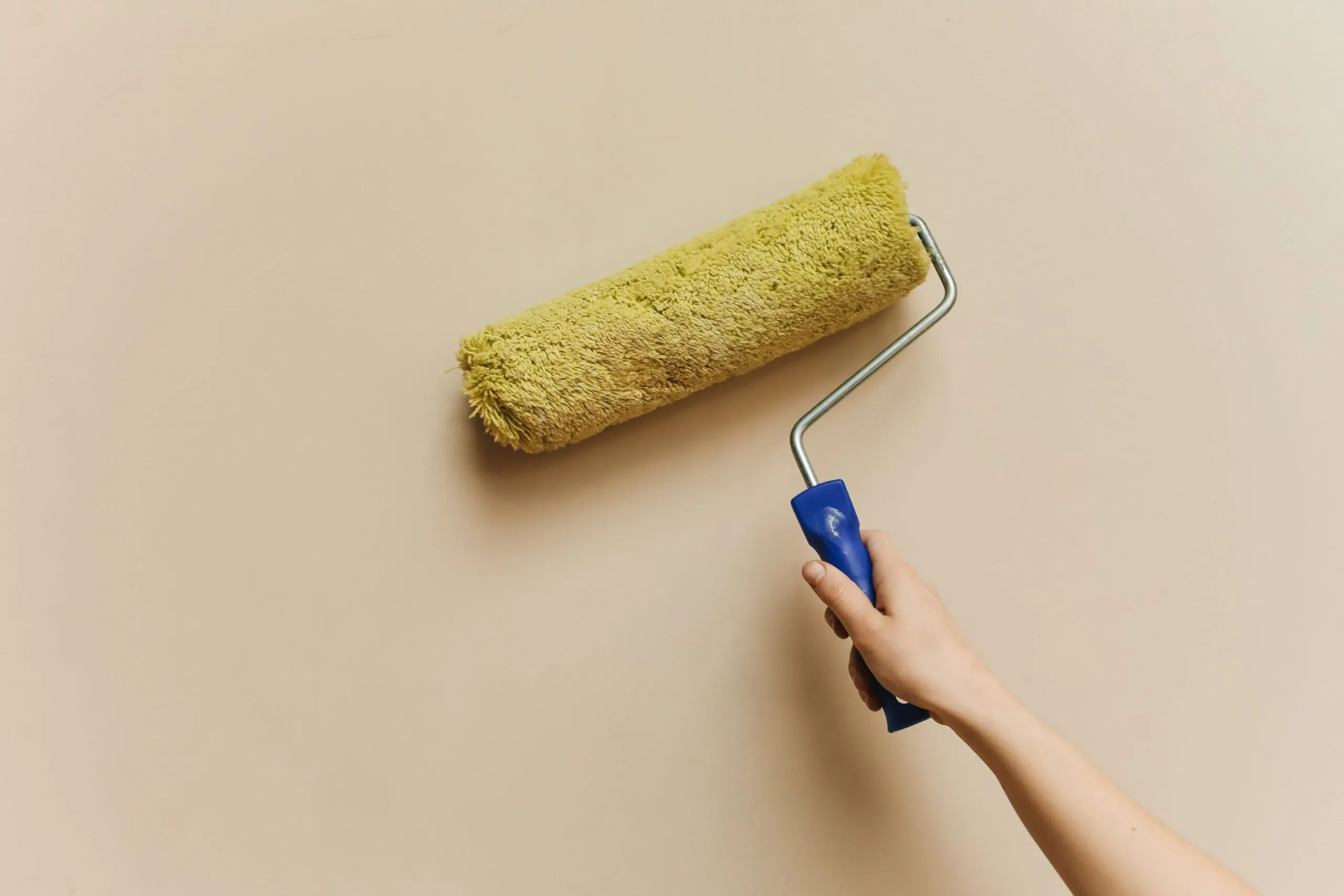 A hand using a yellow paint roller to paint a beige wall. Perfect for DIY and home improvement themes.