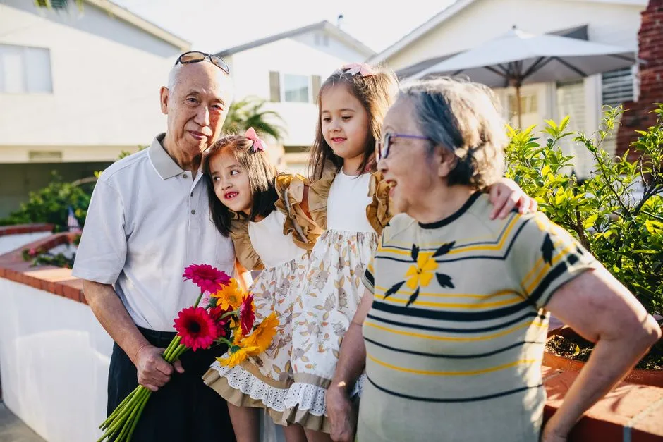 Asian grandparents with twin grandchildren enjoying a sunny day outdoors with flowers.
