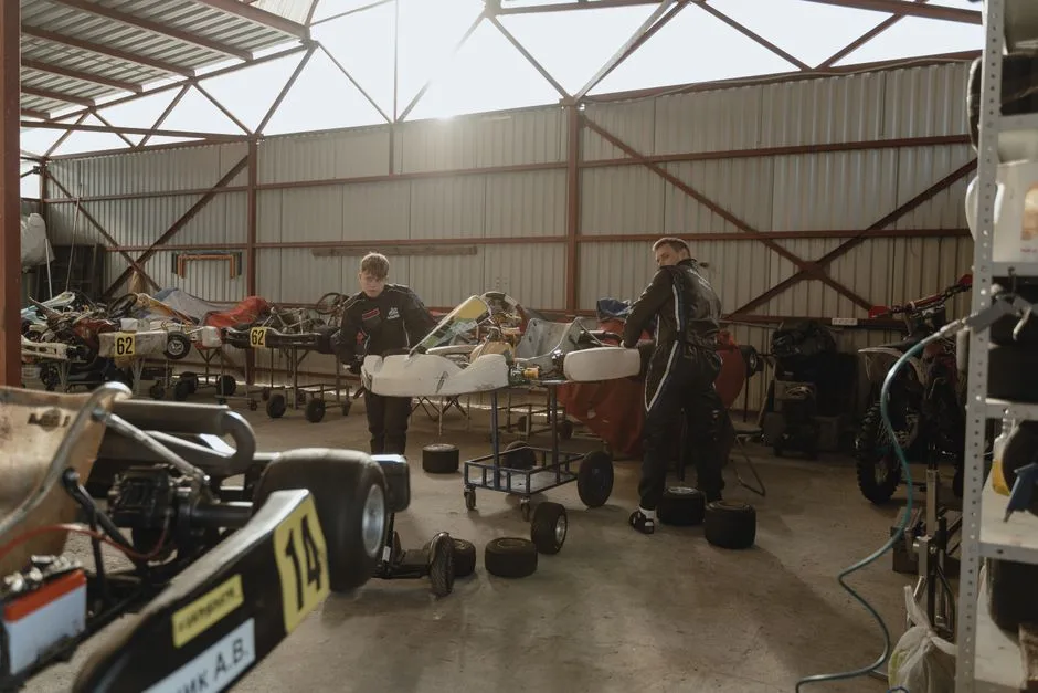 Two mechanics working on go-karts in an indoor workshop with natural lighting.