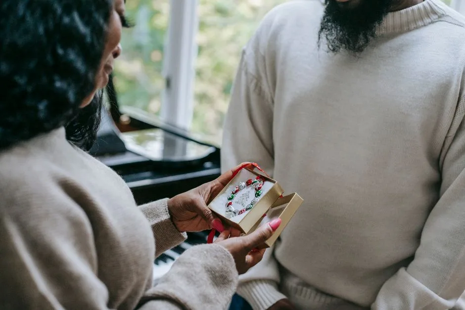 Crop anonymous happy African American couple in sweaters exchanging gifts on blurred background of home