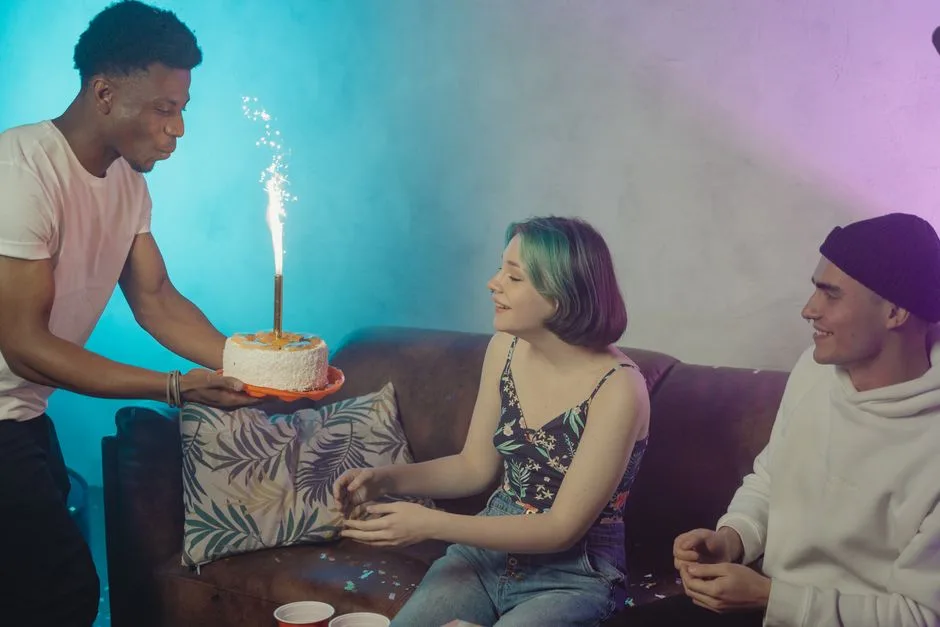 Three friends celebrate a birthday indoors with a lit cake and smiles.