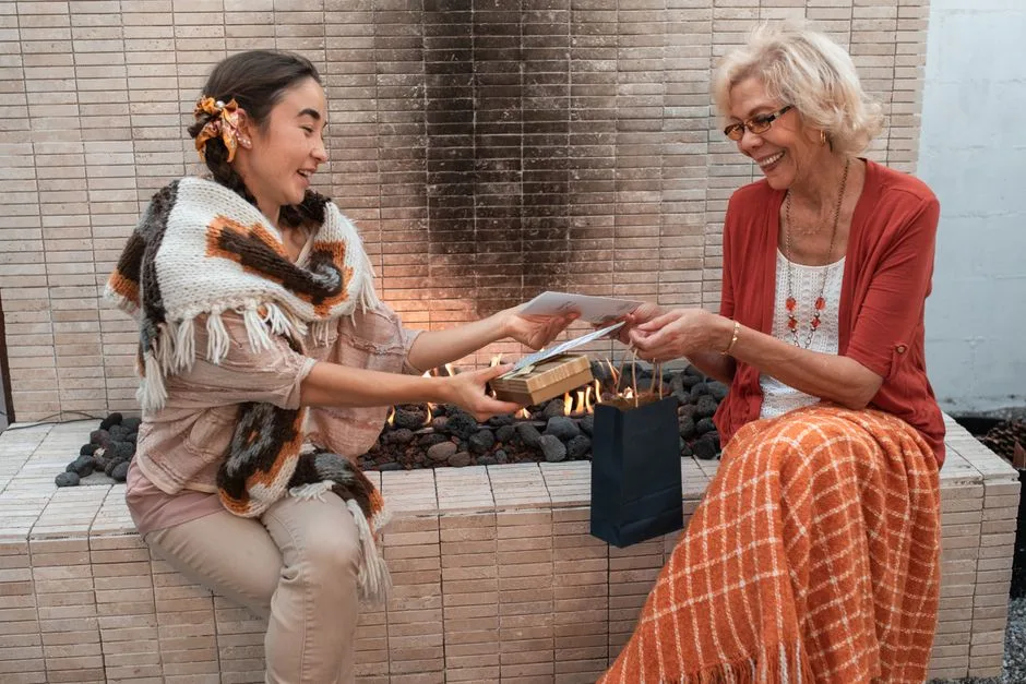 Two women exchanging gifts by an indoor fireplace, embodying warmth and joy.