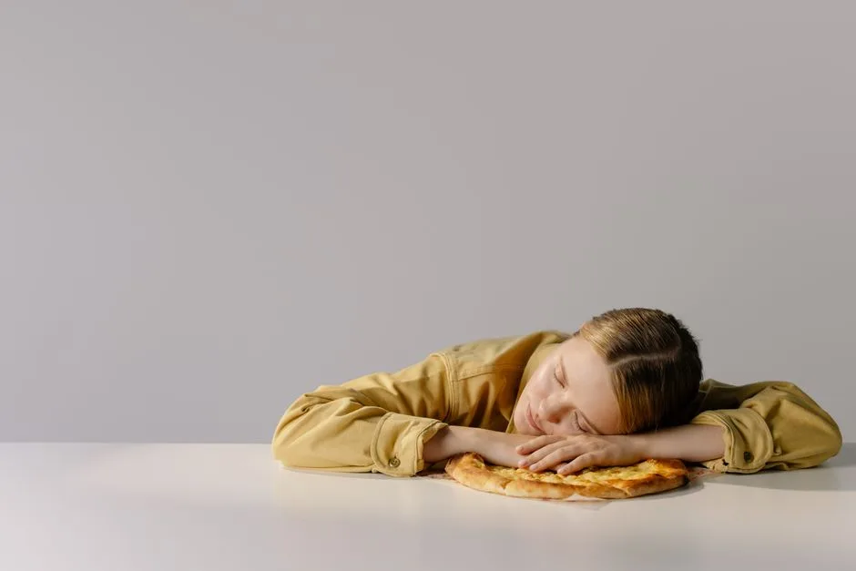 A Caucasian woman with eyes closed, resting her head on a pizza, embodying relaxation and humor.