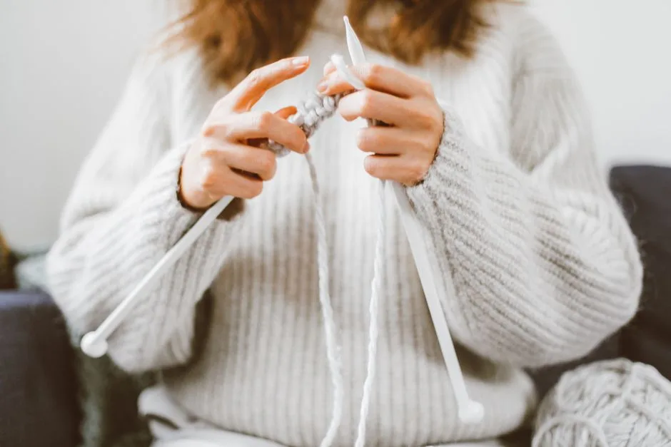 A warm image capturing a woman knitting a sweater indoors wearing a cozy knit sweater.