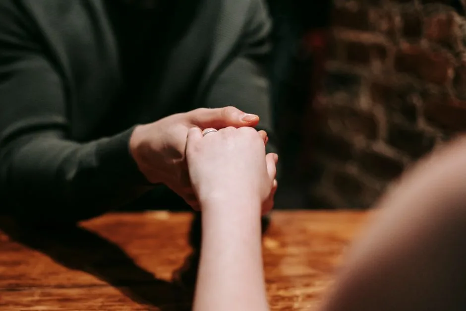 Crop faceless couple sitting at wooden table in light restaurant on romantic date while holding hands with ring on finger