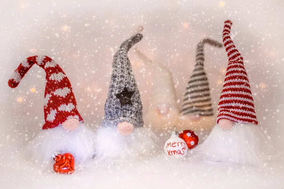 Traditional toy gnomes with colorful hats and beards placed with holiday inscription on bright baubles in snowfall during Christmas celebration
