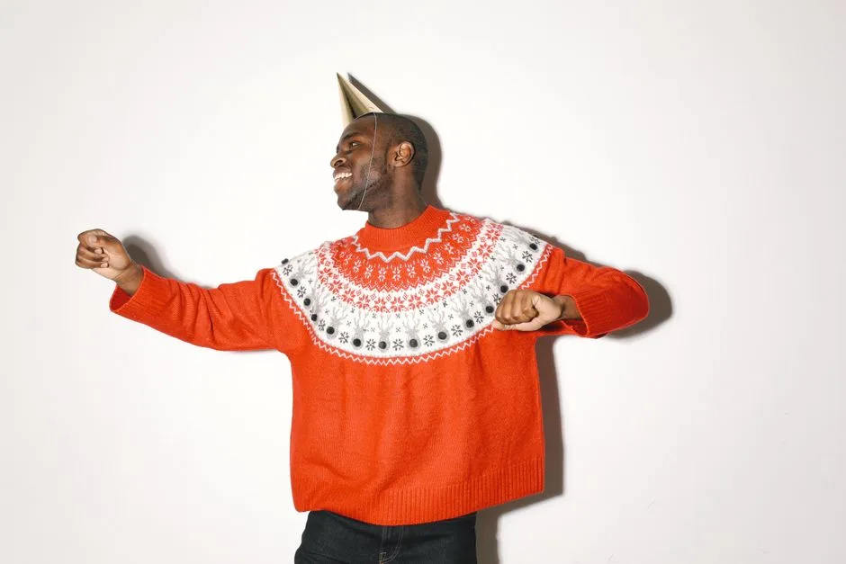 Joyful African American man in a festive sweater and party hat dancing happily.