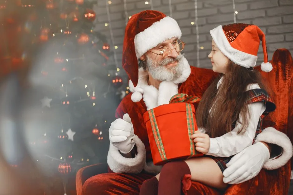 A cheerful girl receives a gift from Santa Claus beside a decorated Christmas tree.