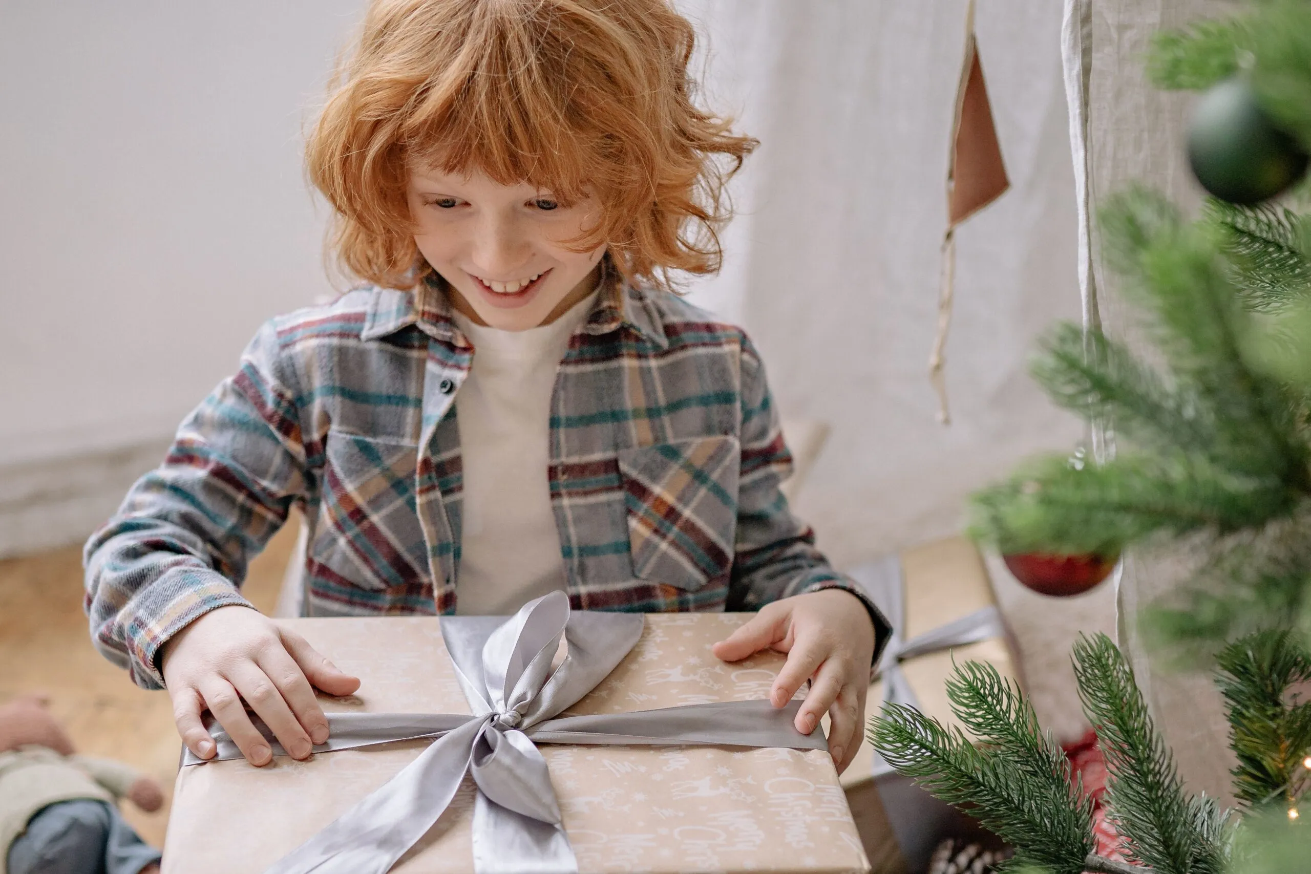 A joyful child eagerly opens a present near a decorated Christmas tree indoors.
