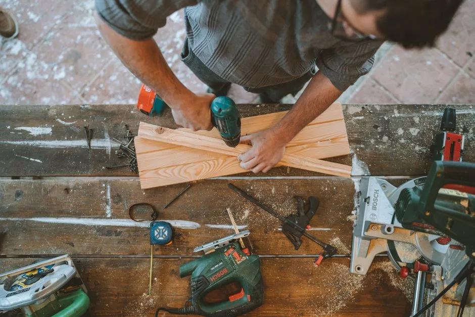 Craftsman busy drilling wooden planks in a carpentry workshop with various tools around.