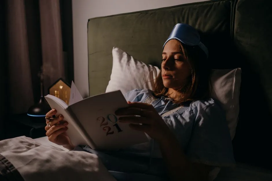 Woman in bed with sleep mask, reading a book, creating a relaxing, cozy atmosphere.