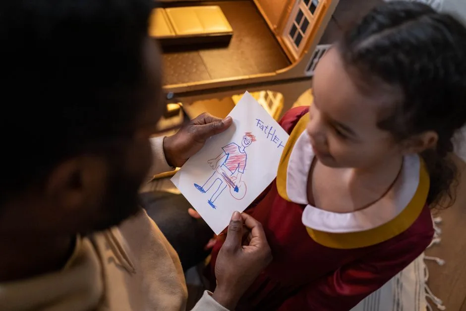 A father and daughter share a touching moment over a child's drawing labeled 'Father'.