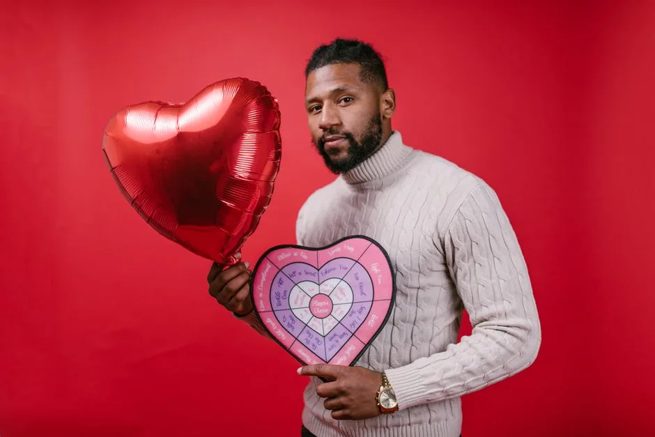 Man holding a heart-shaped balloon and card against a red background, celebrating Valentine's Day.