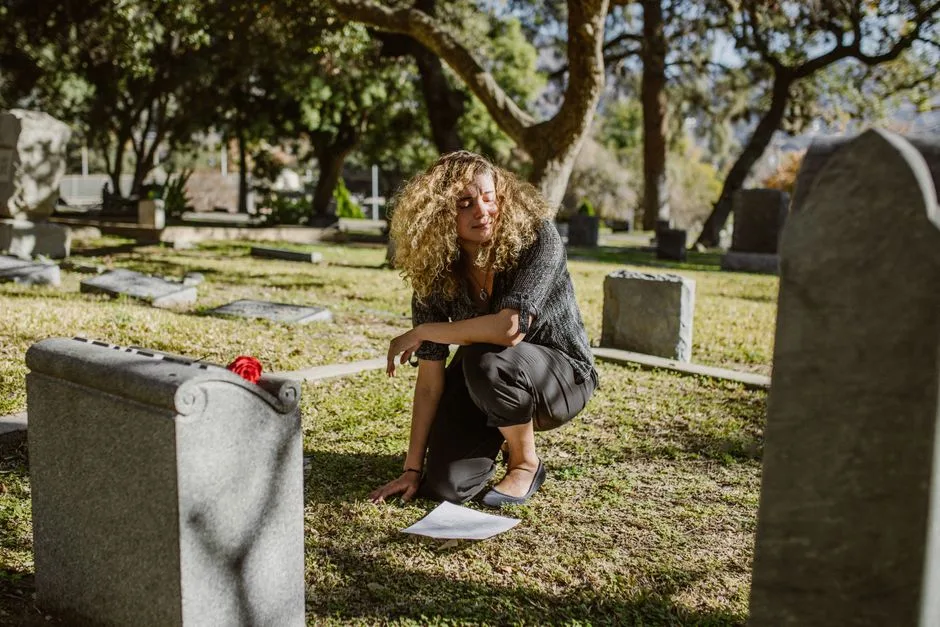 A woman kneeling by a grave in a sunny cemetery, expressing grief and bereavement.